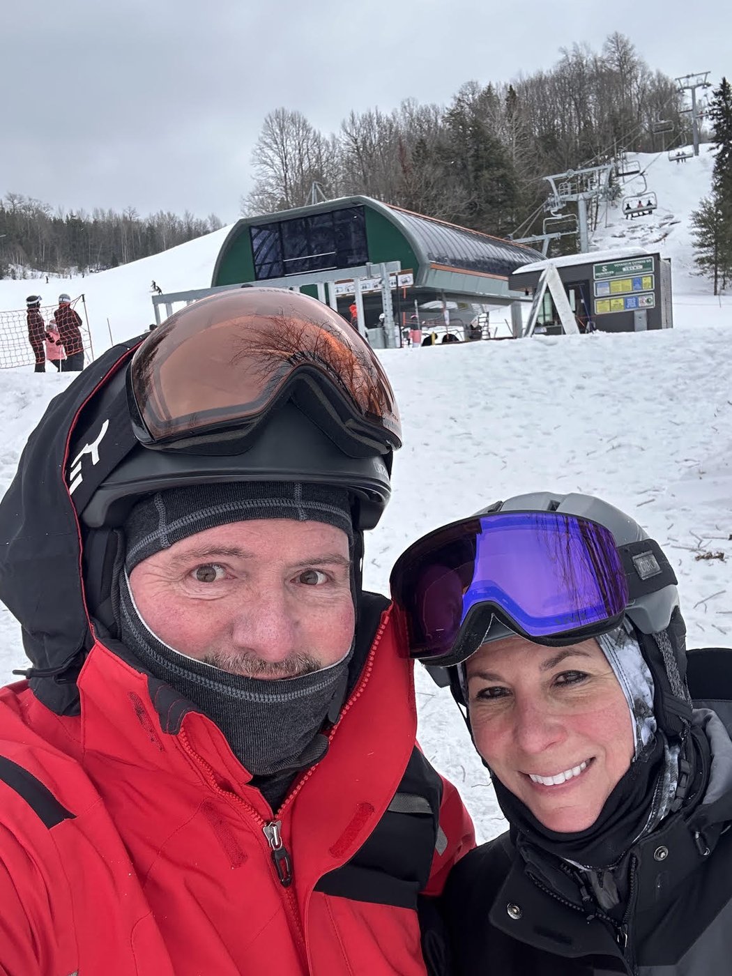 Two skiers in helmets and goggles at a ski hill chairlift