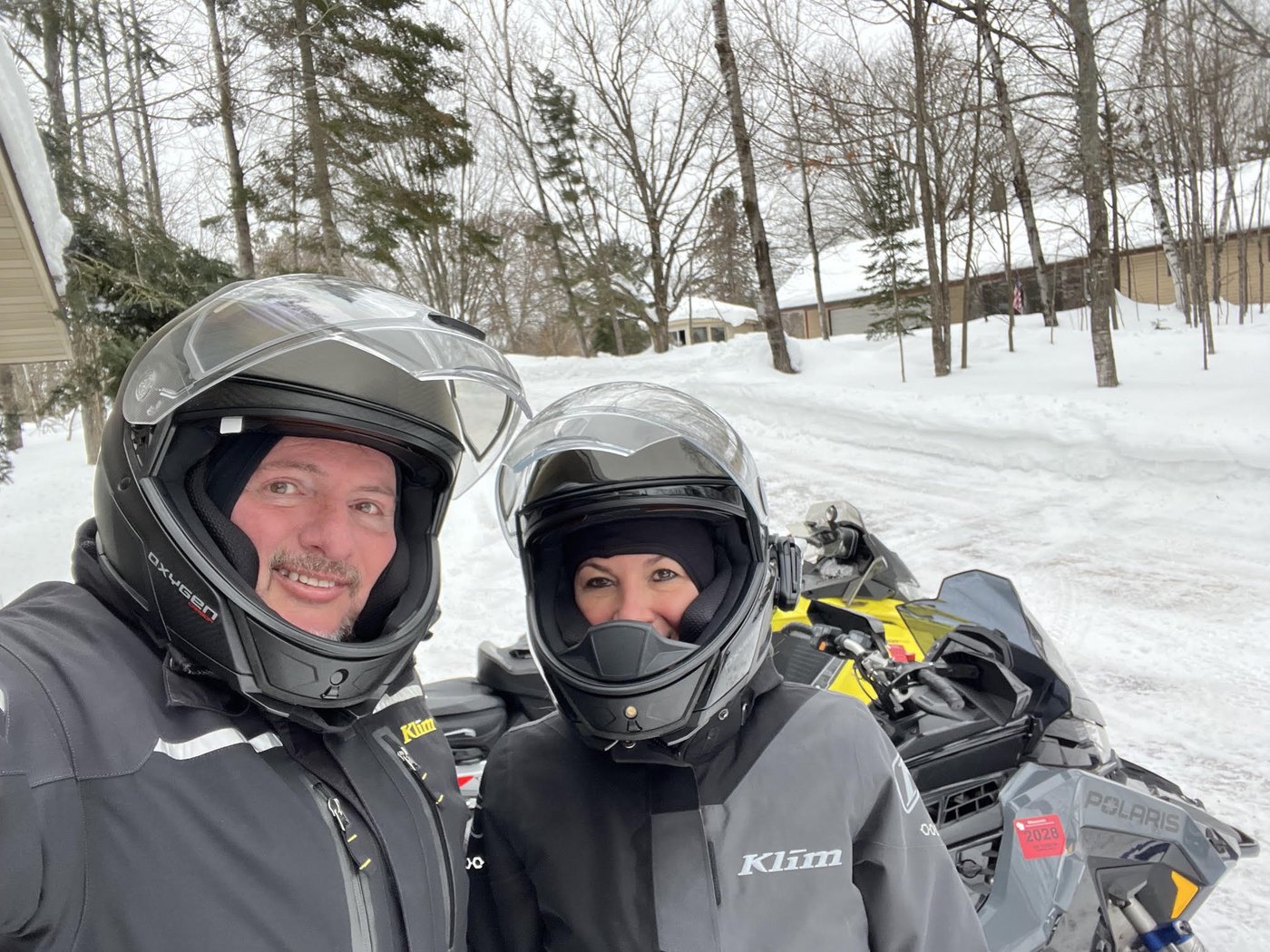Two riders in helmets with a Polaris snowmobile on a snowy road